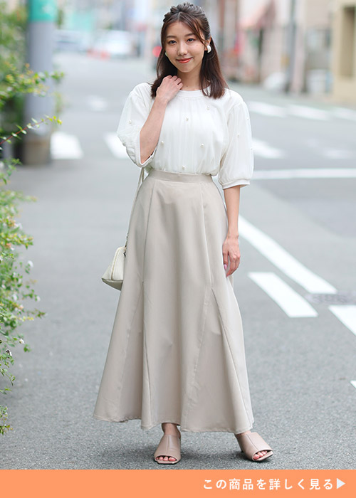 サンドベージュのマーメイドスカートとホワイトブラウスのコーデにベージュサンダルを履く女性