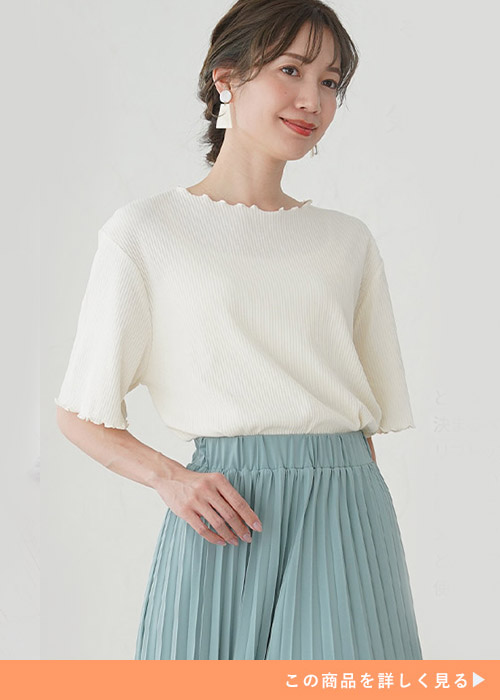 オフホワイトのニットソーにミントグリーンのプリーツスカートを履く女性
