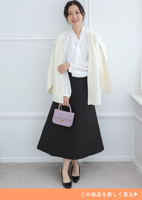 オフホワイトのブラウスとブラックスカートのコーデに白カーディガンを羽織る女性