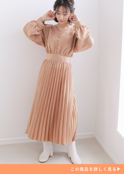 ゴールドの肩タックワンピースにホワイトブーツを履く女性