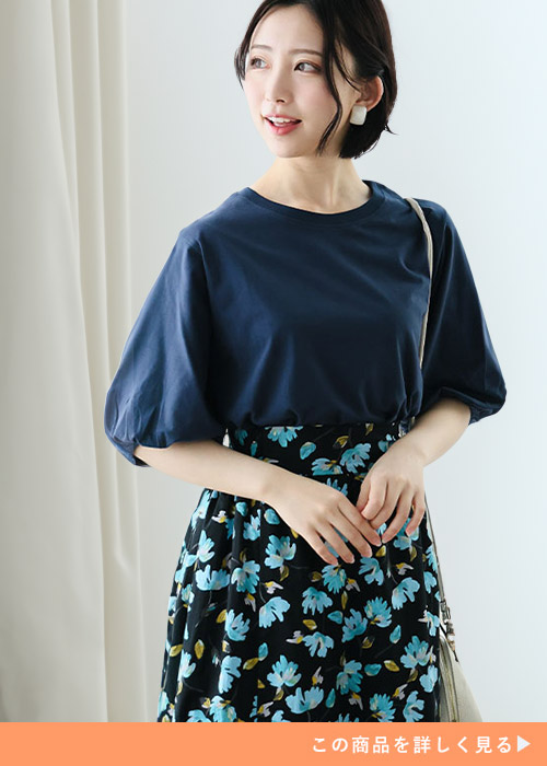 ネイビーのパフ袖のトップスと花柄スカートのコーデにベージュのショルダーバッグを持つ女性