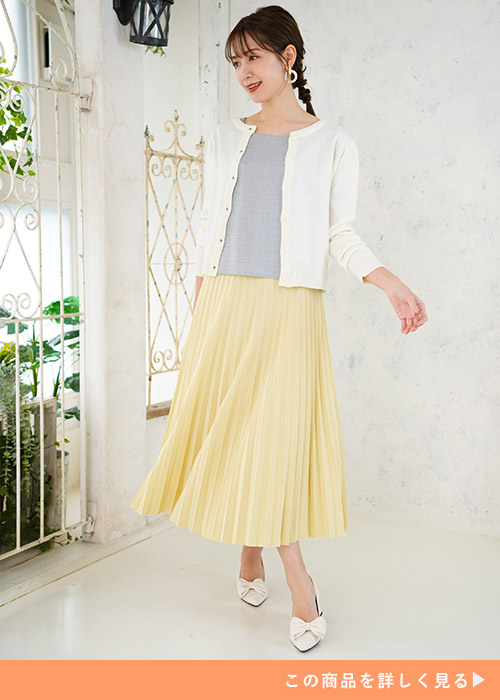 グレーのトップスとフレッシュイエローのプリーツスカートのコーデに白いカーディガンを羽織る女性