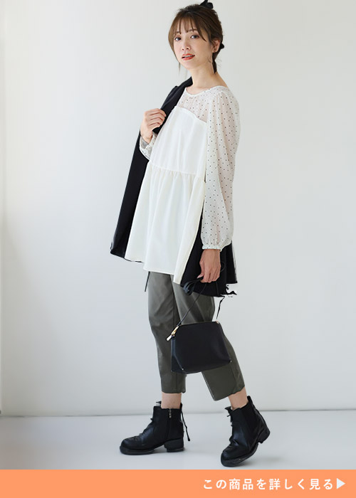 オフホワイトのペプラムトップスとグレーのパンツにブラックのバッグとブーツを合わせる女性