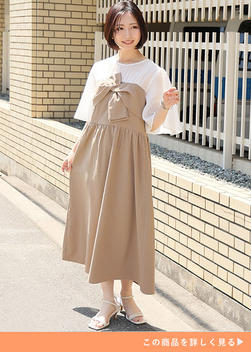 ベージュのツイストリボンのドッキングワンピースにホワイトサンダルを履く女性