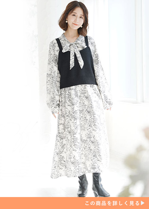 ホワイトの花柄ワンピースとブラックのビスチェのセットアップにブラックブーツを履く女性