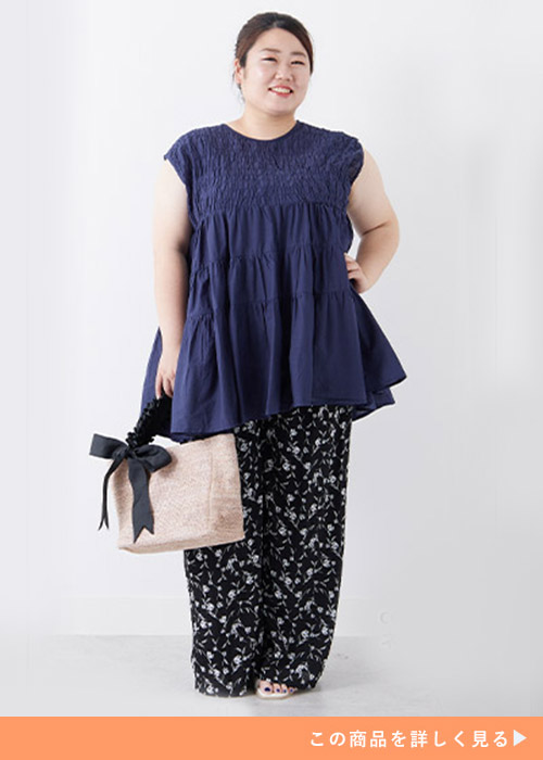 ネイビーのシャーリングチュニックにブラックベースの柄パンツを履く女性
