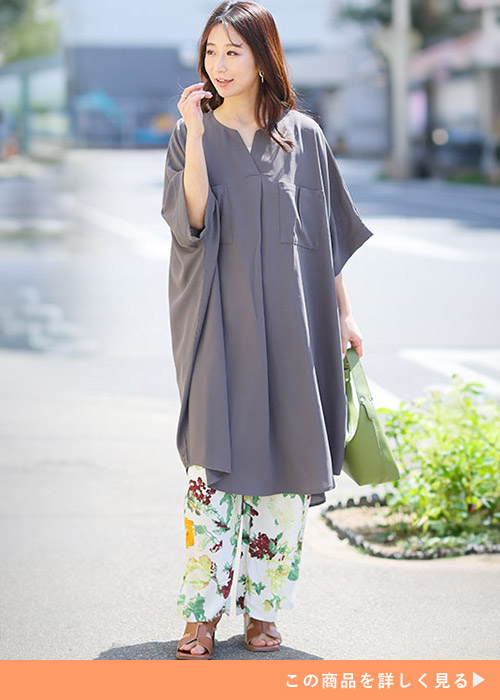 チャコールのロングチュニックとホワイトベースの花柄パンツを履く女性