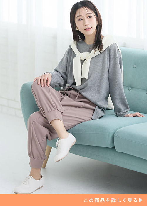 グレージュのジョガーパンツとグレーニットのコーデにホワイトカーデを羽織る女性