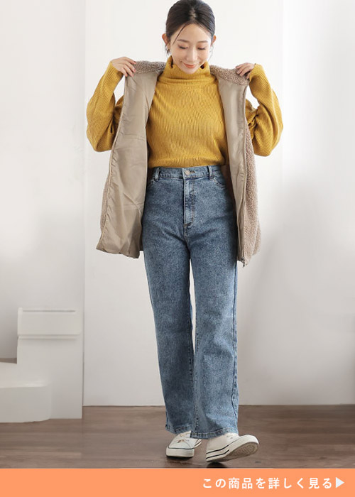 ネイビーケミカルのパンツとマスタードカラーのトップスにボアベストを羽織る女性