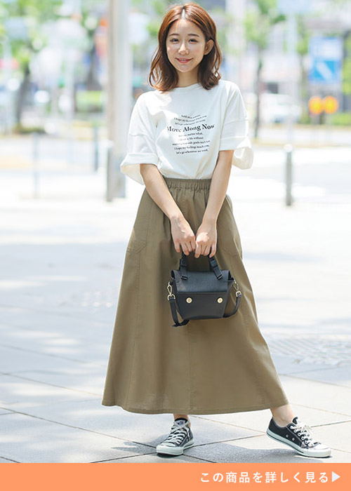 ダークベージュのスカートとホワイトTシャツのコーデにブラックスニーカーとバッグを合わせる女性