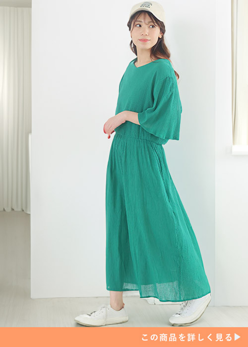 グリーンのワンピースにホワイトスニーカーとキャップを合わせる女性