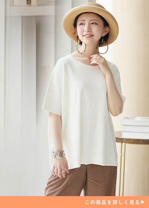 ホワイトサマーニットとブラウンのパンツにバングルとピアスを合わせる女性