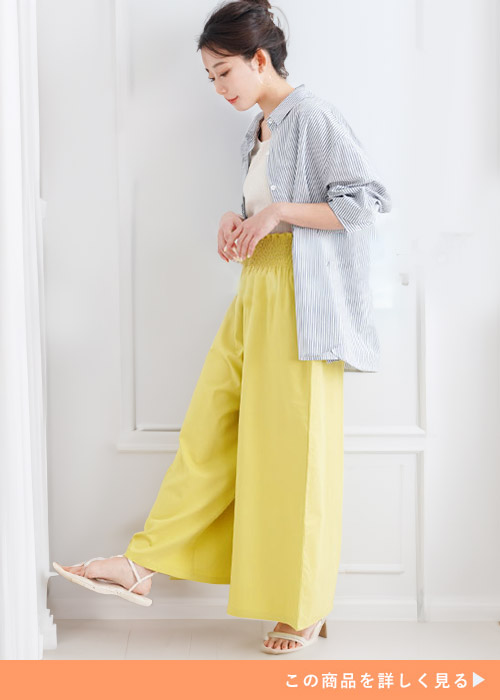 ホワイトトップスとイエローのワイドパンツにストライプシャツを羽織る女性