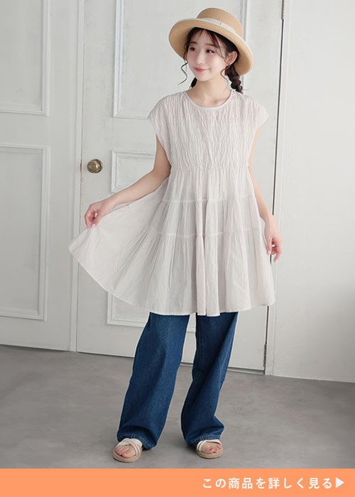 グレージュのティアードチュニックとデニムのコーデにストローハットをかぶる女性