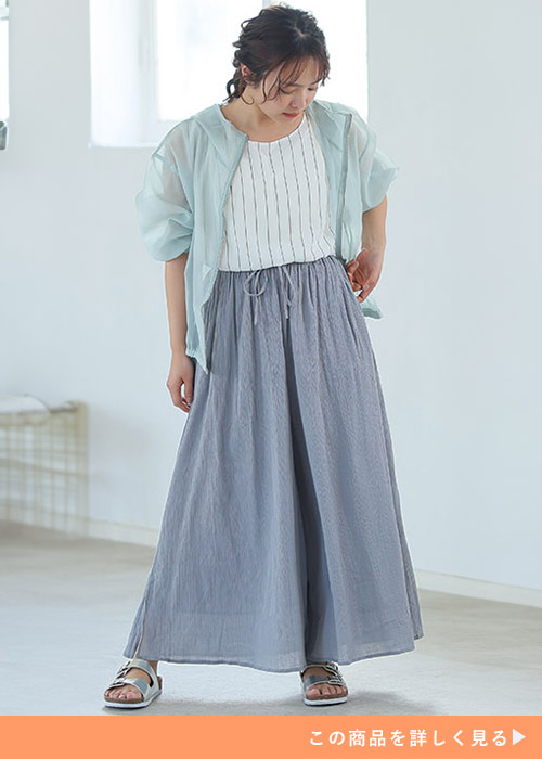 ライトグレーのスカンツとストライプのトップスにライトブルーのシアーシャツを羽織る女性