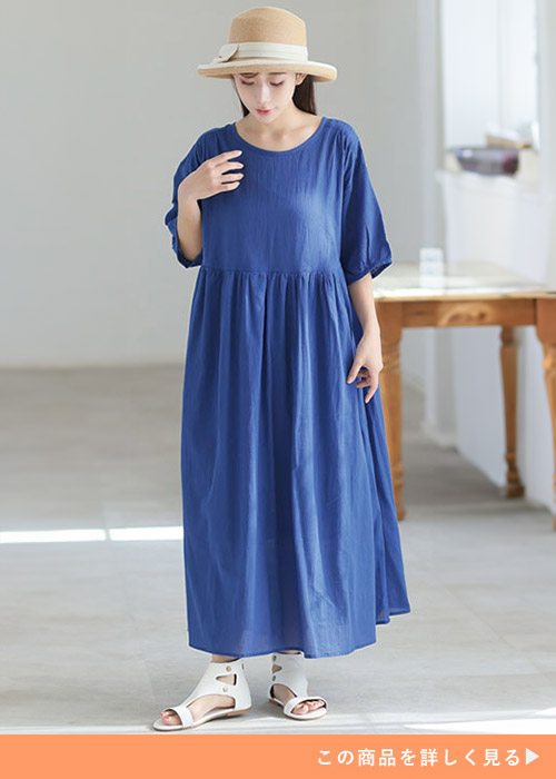 ロイヤルブルーのウエスト切り替えワンピースにサンダルとストローハットを合わせる女性