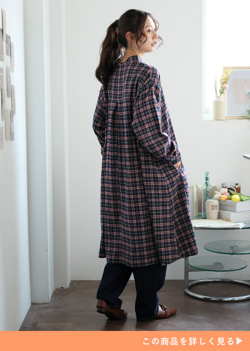 ネイビー×ボルドーのチェック柄ワンピースを着て、下にデニムパンツを履く女性