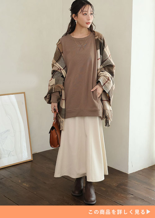 白のスカートにブラウンのトレーナーを合わせ、チェックのストールを羽織る女性