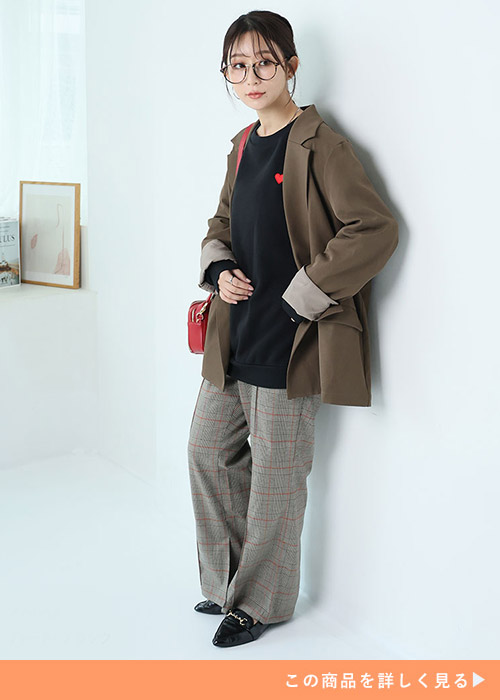 チェックのパンツに黒のトレーナー、茶色のジャケットを羽織る女性