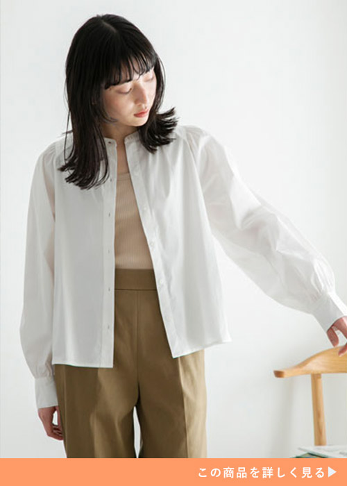 ベージュのインナーとブラウンのパンツのコーデにホワイトの袖ボリュームシャツを羽織る女性
