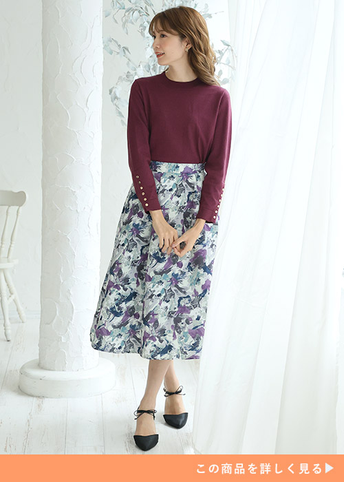 パープルのラメニットと柄スカートのコーデにブラックパンプスを履く女性