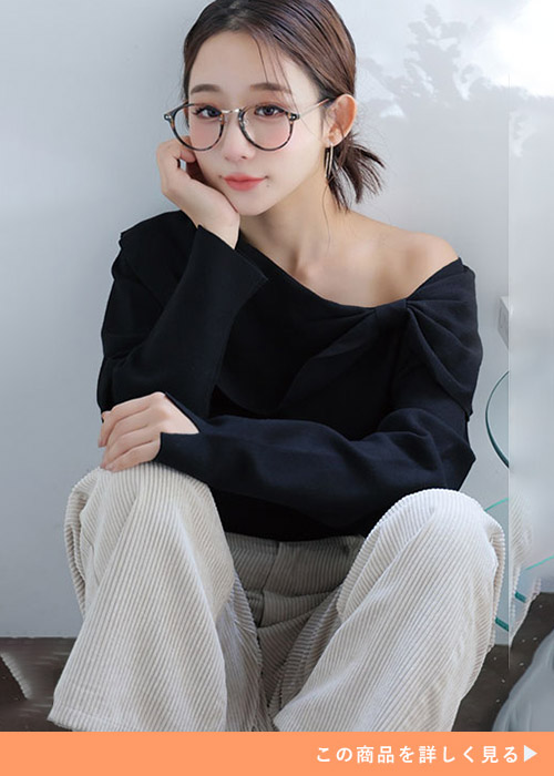 ブラックのオフショルリボントップスとベージュのパンツのコーデの女性