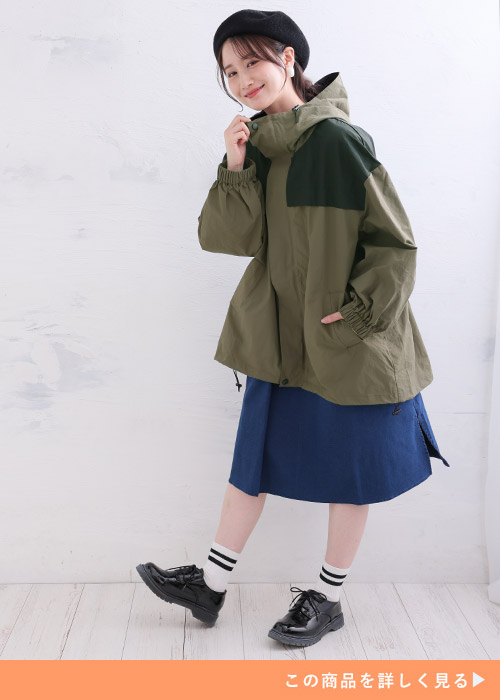 カーキブラウンの配色マウンテンパーカとネイビーのスカートのコーデにブラックローファーを履く女性