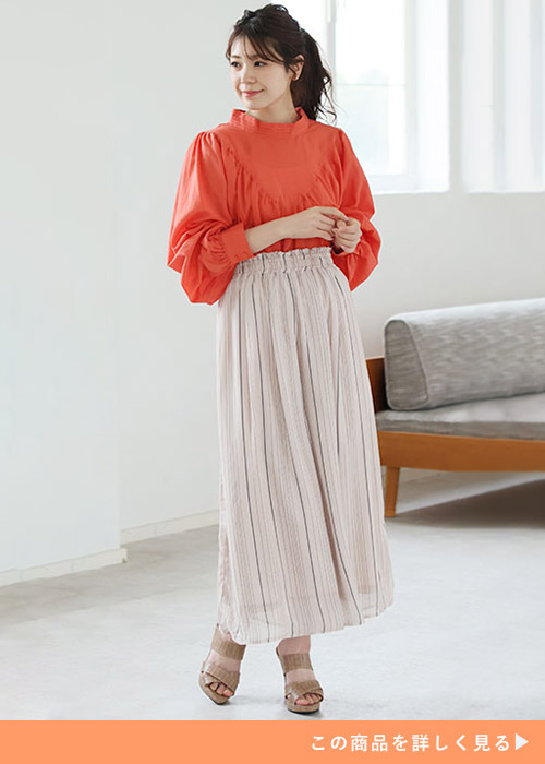 オレンジのギャザーブラウスに細ストライプのスカートを履く女性