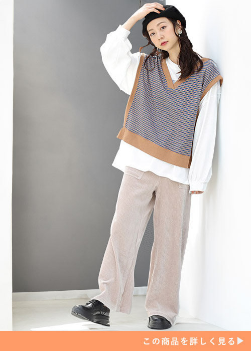 ホワイトトップスとベージュのパンツのコーデにブルーのカットジャガードベストを合わせる女性