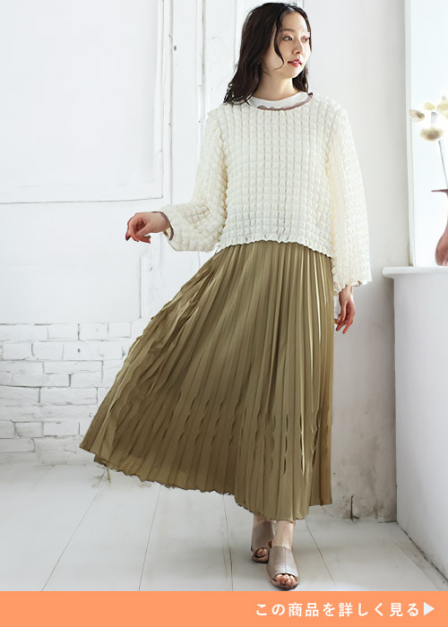 ホワイトトップスとピスタチオカラーのプリーツスカートにベージュのサンダルを履く女性