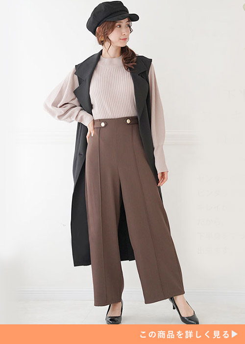 チョコレートブラウンのワイドパンツとベージュニットのコーデにブラックロングジレを羽織る女性