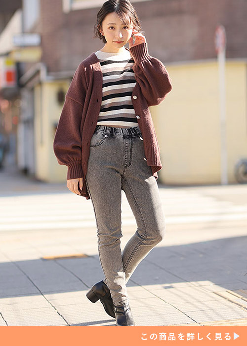 ボーダートップスにブラウンのカーディガンを羽織り、ブラックのスキニーデニムを履く女性