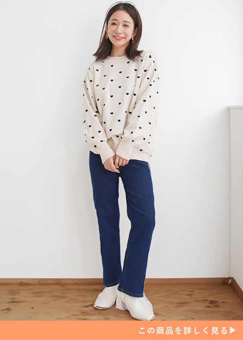 ベージュのハート柄トップス×ネイビーのストレートデニムパンツを着る女性