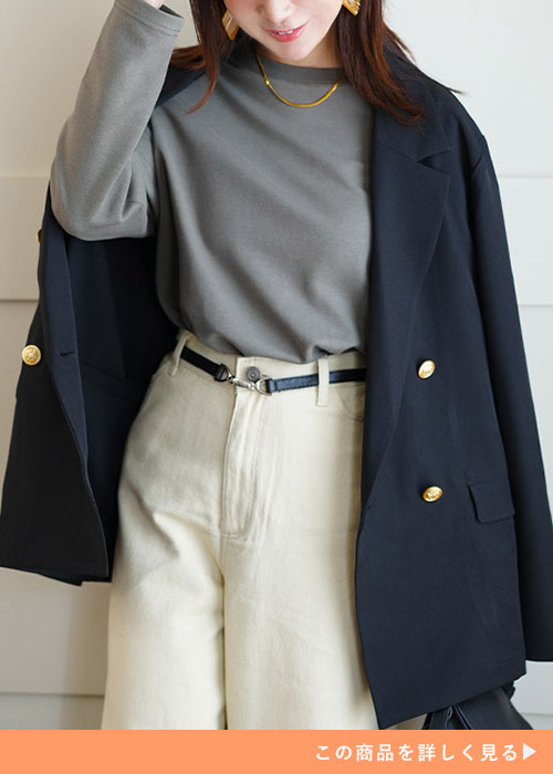 グレーのトップスとホワイトパンツのコーデにネイビーの金ボタンジャケットを羽織る女性