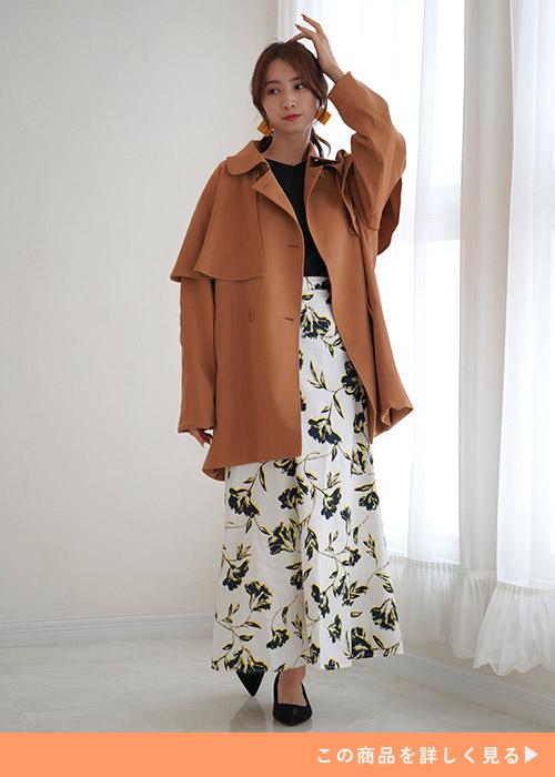 花柄のスカートと黒のトップスにブラウンのジャケットを着る女性