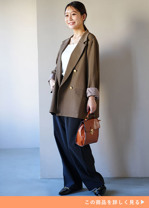 ブラックパンツとホワイトトップスのコーデにブラウンのダブルボタンジャケットを羽織る女性