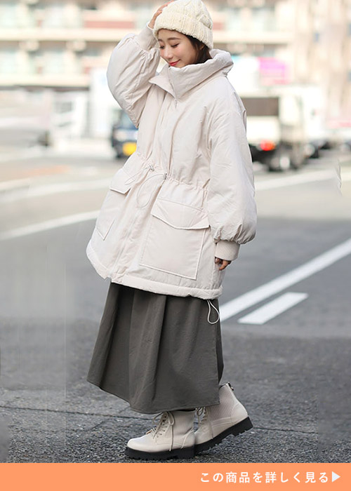アイボリーのウエストドロストコートとグレーのスカートのコーデにアイボリーのニット帽をかぶる女性