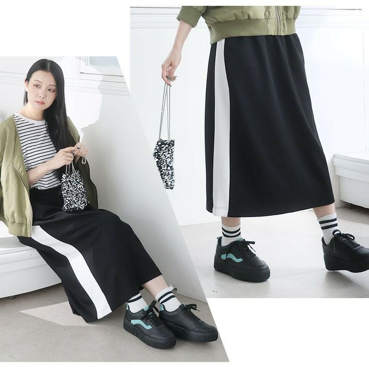異素材切り替えスカートとカーキのジャケットに黒のスニーカーを履く女性