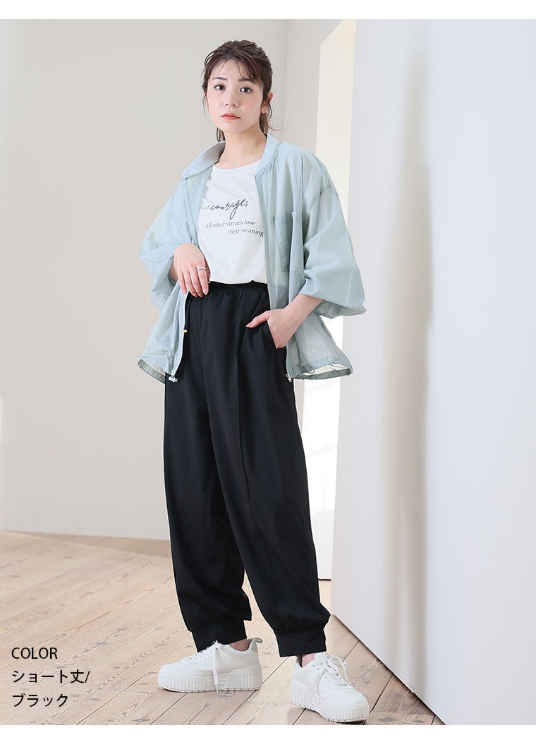 白Tシャツにブルーの薄手ジャケットを羽織って、ブラックのジョガーパンツを履き、スカーフを首に巻く女性