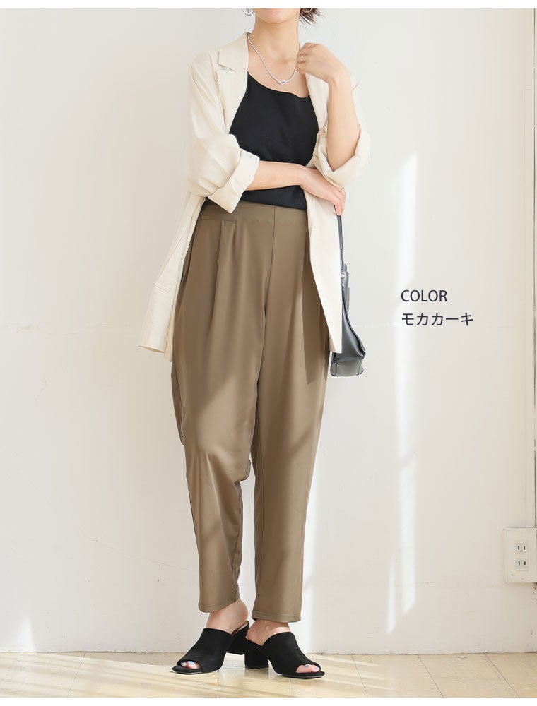 オフホワイトのジャケットとモカカーキのテーパードパンツのコーデに黒のサンダルを履く女性